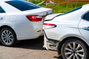 Two white cars involved in a collision on a city street while reversing.