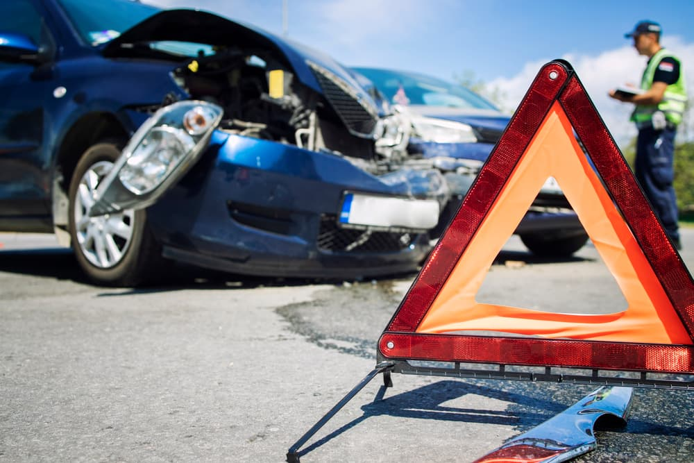 Damaged blue car after an accident with a warning triangle in foreground.