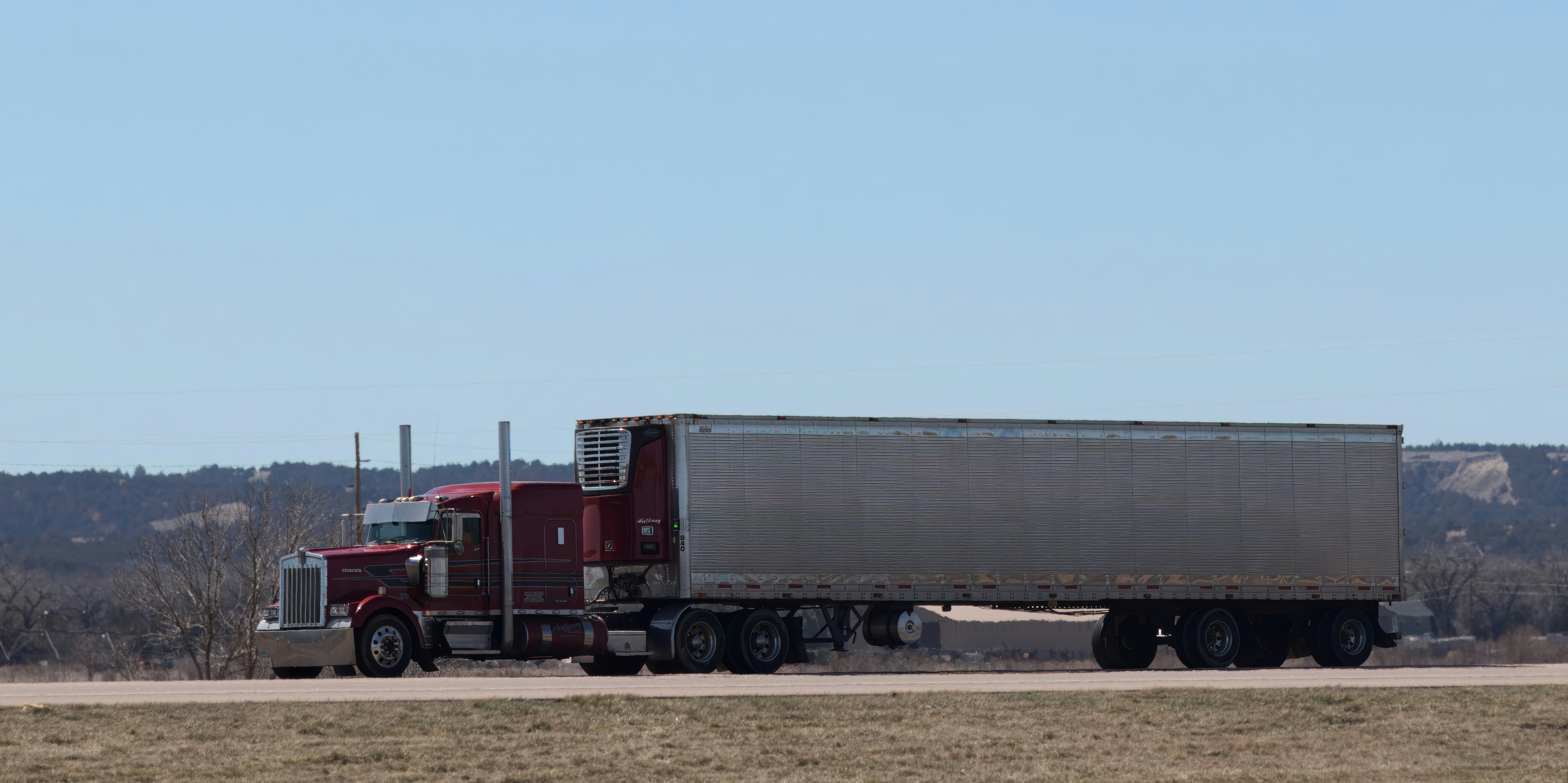 A long tractor-trailer drives down an otherwise empty highway. The cab is red.