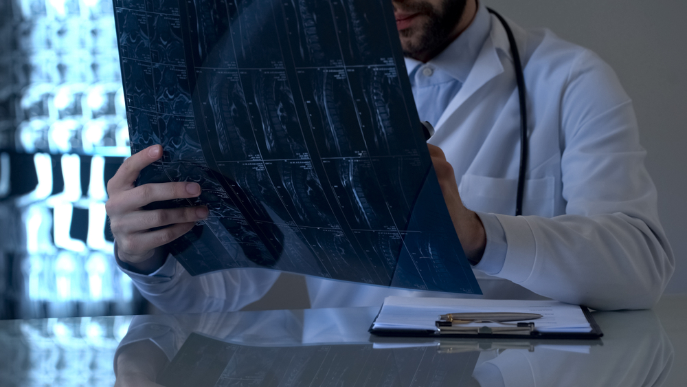 A male doctor examines a medical chart while standing in a clinical setting.