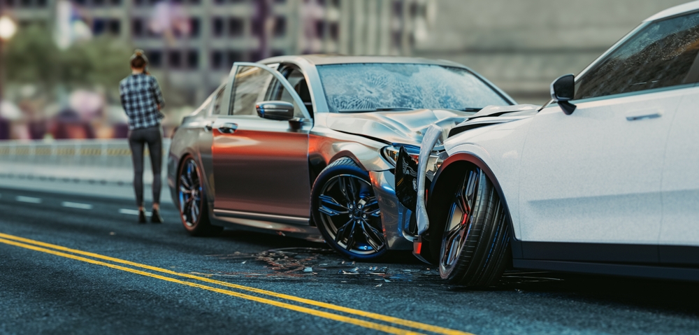 A damaged car shows visible dents and scratches after colliding with another vehicle on the road.
