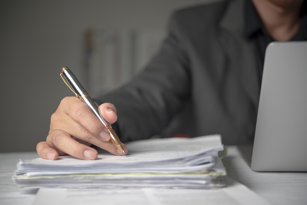 Person writing on a stack of papers next to a laptop